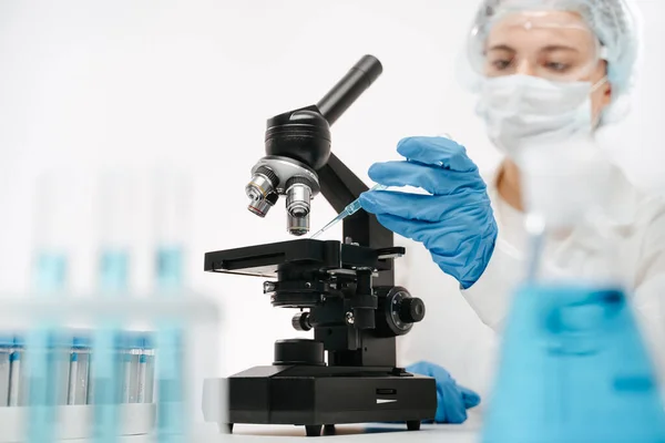 Klinikte koronavirüs testi yapmak için mikroskopla çalışan kadın asistan.