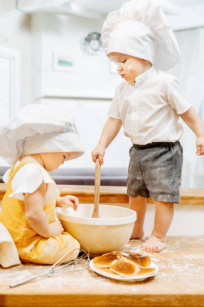 Charming grimy caucasian children cook dough in white cap