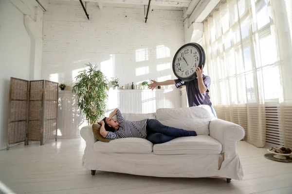 Mannen-clock vakna flickan som ligger på soffan i loftet. Stockbild