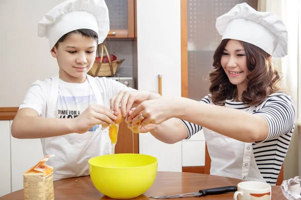 Moeder en haar kind in witte chef-kok hoeden voorbereiding een omelet in de keuken. — Stockfoto
