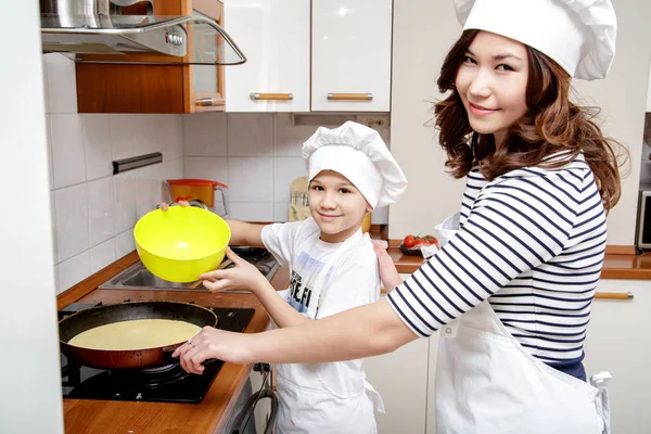 Moeder en haar zoon in witte chef-kok hoeden voorbereiding een omelet in de keuken. — Stockfoto