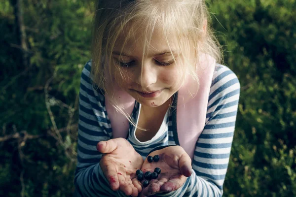 Niña de pie en el bosque con la boca manchada sostiene arándanos — Foto de Stock