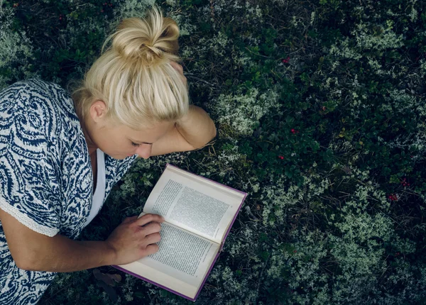 Young beautiful girl lies in the woods on the grass and reading a book.