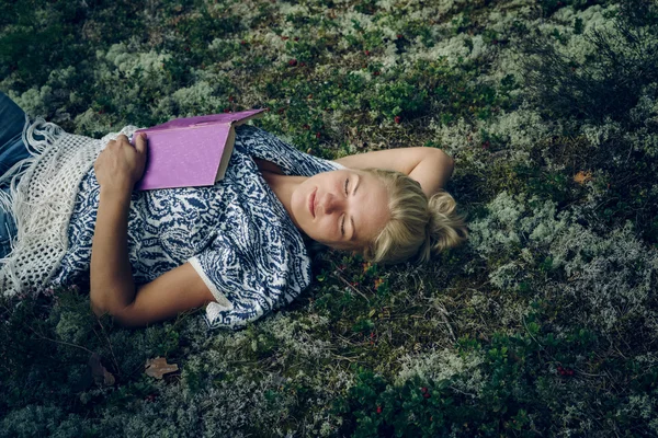 Junges schönes Mädchen liegt im Wald auf dem Gras und liest ein Buch. — Stockfoto