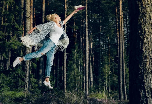 Young beautiful woman reading a book and levitates in the forest