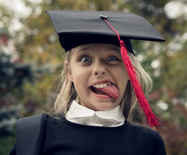 Bella ragazza bionda in uniforme scolastica e cappello di laurea sulla testa sporge la lingua come Albert Einstein . — Foto Stock