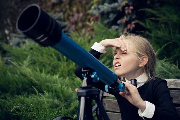 Menina loira bonita em um uniforme escolar no parque olhando através do telescópio Imagens De Bancos De Imagens Sem Royalties