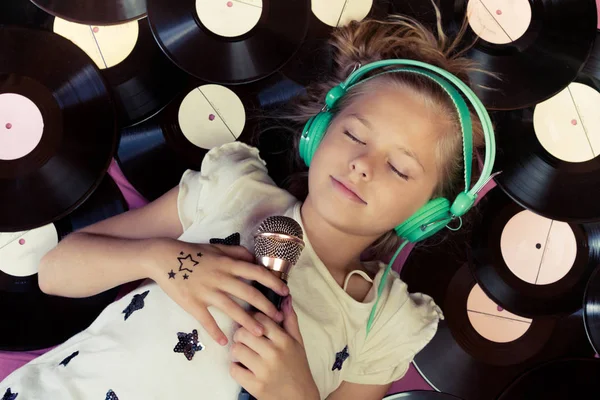 Güzel kız tutarak bir mikrofon ve kulaklıklar müzik vinil kayıtların yanındaki yalan.