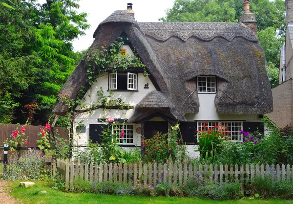 Reetgedeckte Hütte mit weißen Wänden und buntem Garten. — Stockfoto