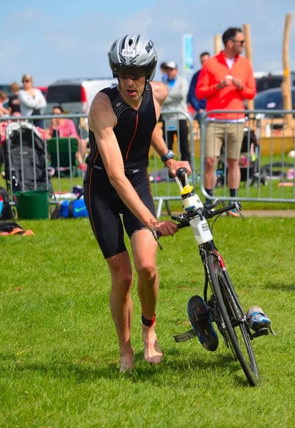 Male triathlete at end of cycling stage with bicycle. — Stock Photo, Image