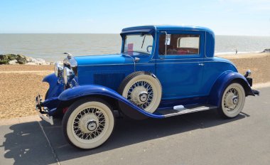  Deniz kıyısındaki beyaz duvar lastikler ile Vintage mavi otomobil park.