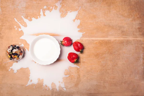 Teller mit verschütteter Milch, Erdbeeren und Nüssen auf hölzernem Backgro — Stockfoto