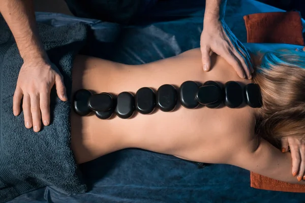 Массажист делает массаж с целебными камнями для женского позвоночника — стоковое фото