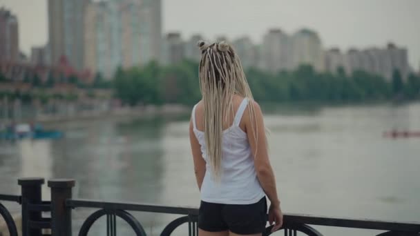 Молодая блондинка с косичками на берегу реки — стоковое видео
