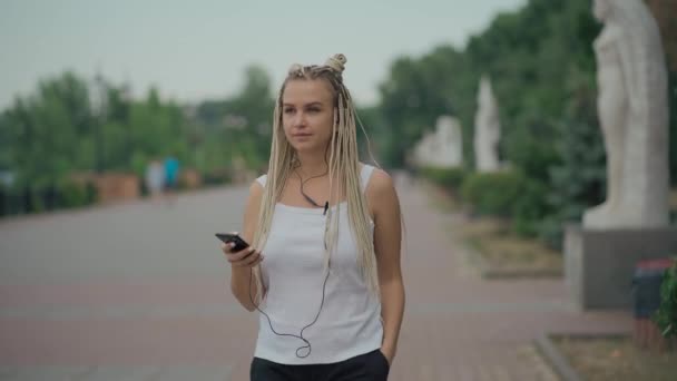 Ung blond flätad kvinna gå på gatan och lyssna musik — Stockvideo