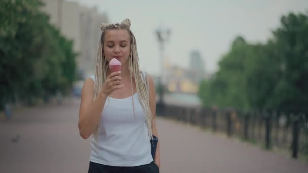 Gevlochten blonde vrouw eten koud roze ijs in park — Stockvideo