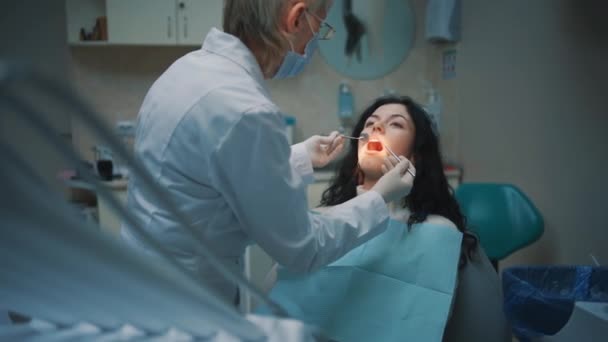 Dentista profesional mujer comprobar diente de joven morena hembra — Vídeos de Stock