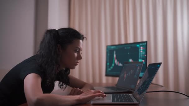 Comerciante femenino joven con el ordenador portátil y la pantalla mirando gráficos de stock — Vídeo de stock