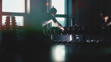 Mükemmel gövdeli atletik adam spor salonunda dambıllarla egzersiz yapıyor.