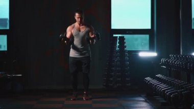 Mükemmel gövdeli atletik adam spor salonunda dambıllarla egzersiz yapıyor.