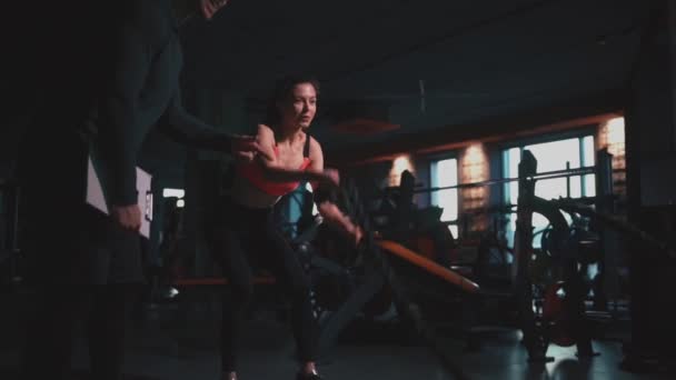 Athletic female exercising ropes in modern gym with personal trainer — Stock Video