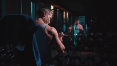 Mükemmel gövdeli atletik adam spor salonunda dambıllarla egzersiz yapıyor.