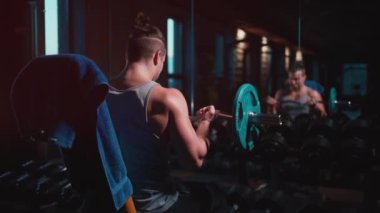 Mükemmel gövdeli atletik adam spor salonunda dambıllarla egzersiz yapıyor.