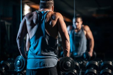 Genç sporcu modern spor salonunda dambılla fiziksel antrenman yapıyor.