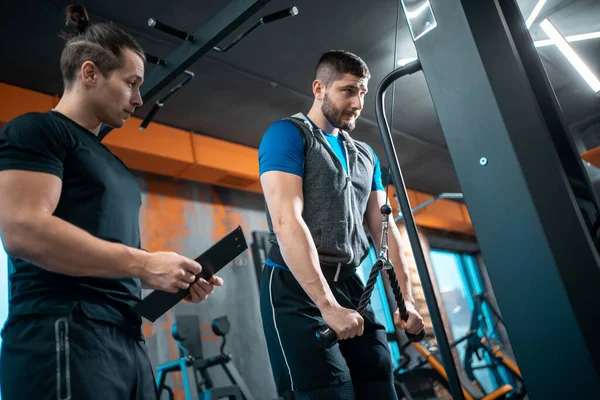 Young man has workout with personal trainer in modern gym — Stock Fotó