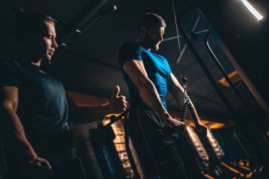 young man has workout with personal trainer in modern gym