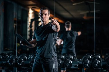 young cheerful personal trainer in gym and with clipboard and stopwatch