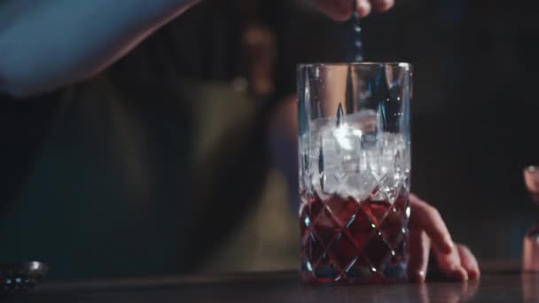 Бармен смешивает классический коктейль негрони с ромом и льдом — стоковое видео