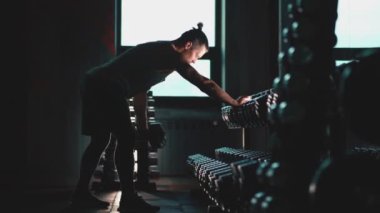 Mükemmel gövdeli atletik adam spor salonunda dambıllarla egzersiz yapıyor.