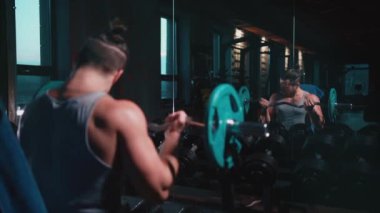 Mükemmel gövdeli atletik adam spor salonunda dambıllarla egzersiz yapıyor.