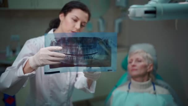 Professionele tandarts vrouw tonen panoramische mond x-ray beeld aan patiënt — Stockvideo