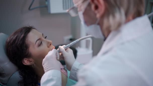 Bela morena encaracolado feminino dentista tratar paciente na clínica moderna — Vídeo de Stock