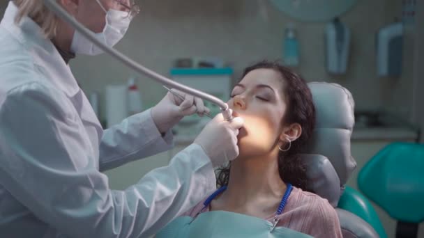 Mooie brunette krullend vrouwelijke tandarts behandelen patiënt in moderne kliniek — Stockvideo