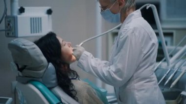 Profesyonel dişçi kadın. Genç esmer kadının dişlerini kontrol ediyor.