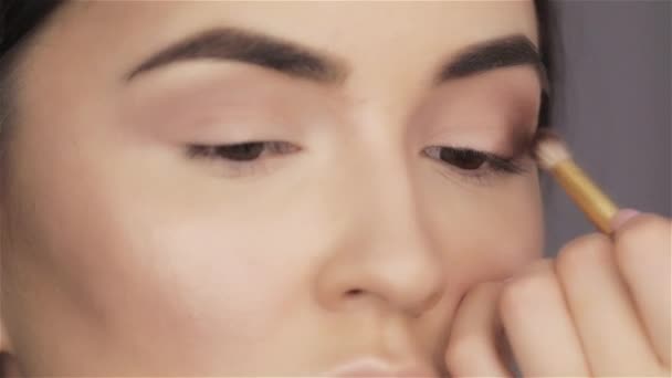 Make up artista dipinge ombre occhi di bella bruna giovane donna primo piano — Video Stock