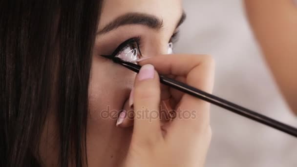 Makeup artist paints the eyes of beautiful young brunette woman close-up — Stock Video