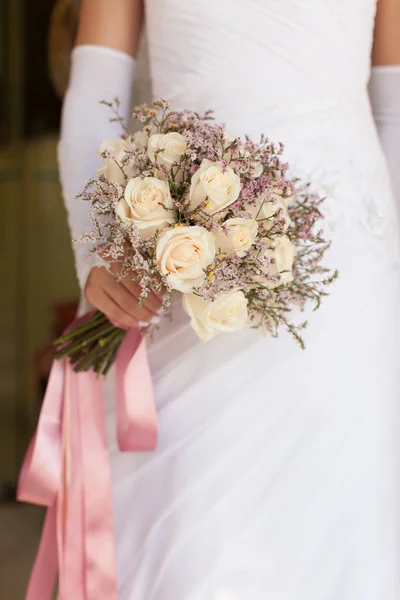 Noiva em vestido branco segurando um buquê de casamento de rosas — Fotografia de Stock