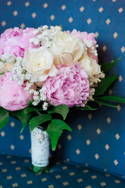 Trouwringen op een boeket van pioenrozen en rozen op een blauwe achtergrond — Stockfoto