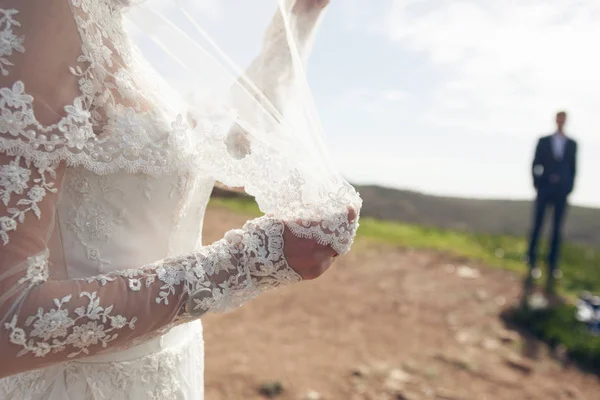 Bruden håller en slöja och stå nära brudgummen — Stockfoto