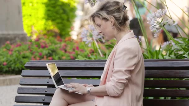 Aantrekkelijke blonde witte vrouw werken freelance met laptop en smartphone in park op zonnige dag — Stockvideo