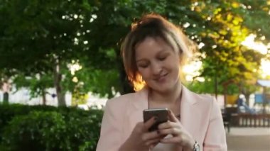 Çekici genç kadın parkta yürüyüş ve bir akıllı telefon kullanır