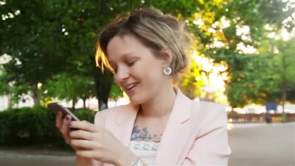 Atractiva joven mujer caminando en el Parque y utiliza un teléfono inteligente — Vídeo de stock