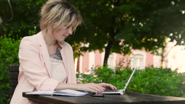 Belle femme blanche blonde travaillant en freelance avec ordinateur portable et smartphone dans le parc à la journée ensoleillée — Video