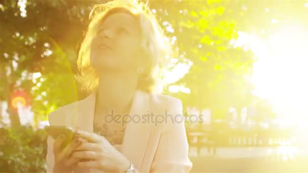 Attraente giovane donna che cammina nel parco e utilizza uno smartphone — Video Stock