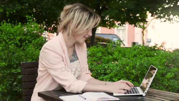 パソコンとスマート フォンで晴れた日に公園の魅力的な金髪白人女性フリーランス — ストック動画