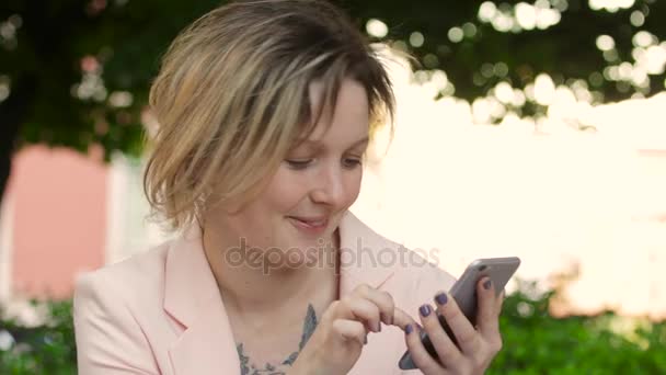 Atractiva rubia blanca trabajando freelance y usando smartphone en el parque en un día soleado — Vídeo de stock